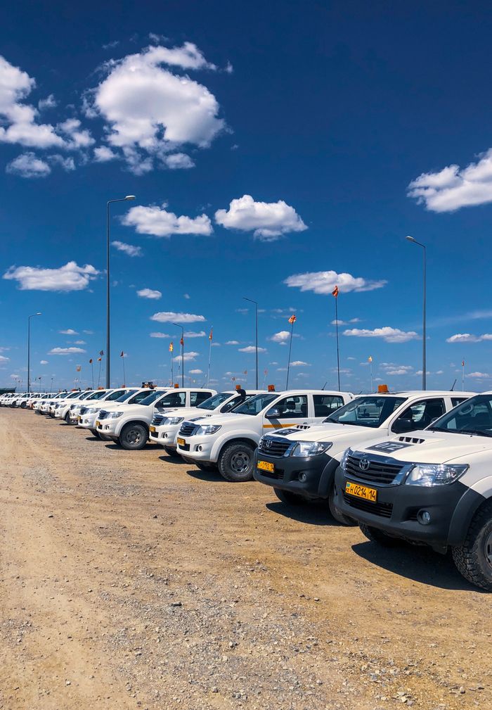 A row of white SUVs parked under a bright blue sky in a Kazakhstan parking lot with desert landscape.